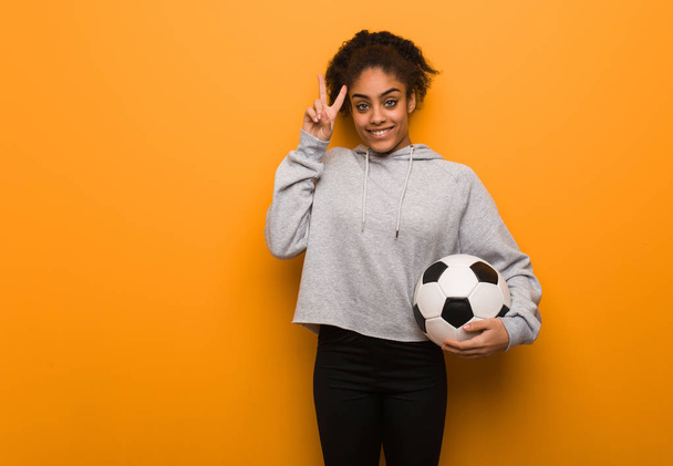 Молодая фитнес черная женщина весело и счастливо делает жест победы. Холдинг футбольный мяч
. - Фото, изображение