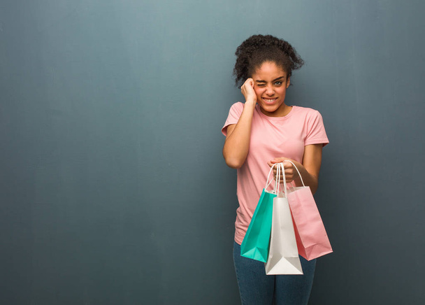 Mujer negra joven cubriendo las orejas con las manos. Ella está sosteniendo una bolsa de compras
. - Foto, imagen