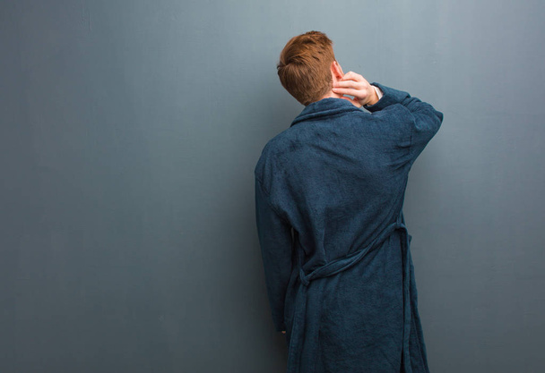 jonge roodharige man in pyjama van achteren denken over iets - Foto, afbeelding