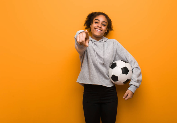 Молодая фитнес черная женщина веселая и улыбающаяся. Холдинг футбольный мяч
. - Фото, изображение