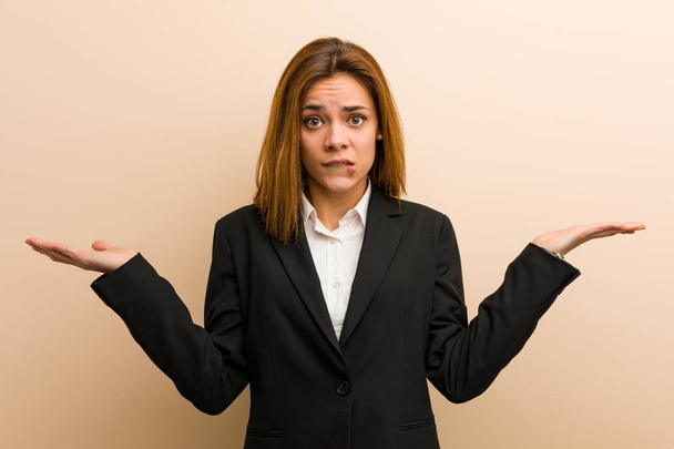 Young caucasian business woman confused and doubtful raising her hands to hold a copy space. - Photo, Image