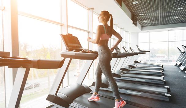 Young woman doing cardio training on treadmill near window - Photo, Image