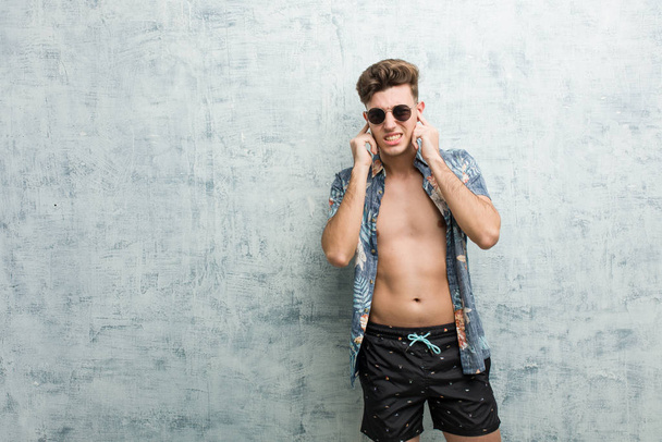 Young caucasian man wearing a swimsuit covering ears with his hands. - Photo, Image