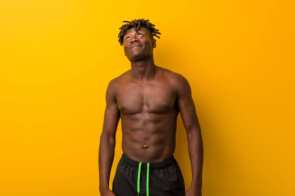 Nuori musta mies paidaton yllään uimapuku haaveilee tavoitteiden saavuttamiseksi ja tarkoituksiin
 - Valokuva, kuva