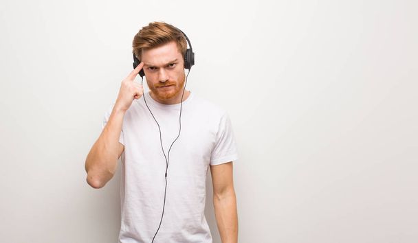 Young redhead man thinking about an idea. Listening to music with headphones. - Photo, Image