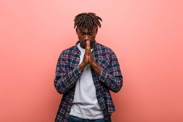 Młody afrykański czarny mężczyzna trzymając się za ręce w modlitwie blisko ust, czuje się pewnie. - Zdjęcie, obraz