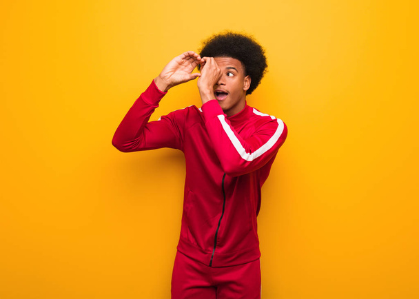 Young sport black man over an orange wall making the gesture of a spyglass - Foto, imagen
