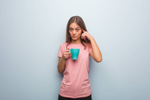 Young pretty caucasian woman thinking about an idea. She is holding a mug. - 写真・画像