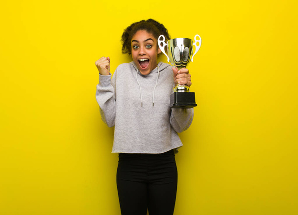 Young fitness black woman surprised and shocked. Holding a trophy. - Foto, afbeelding