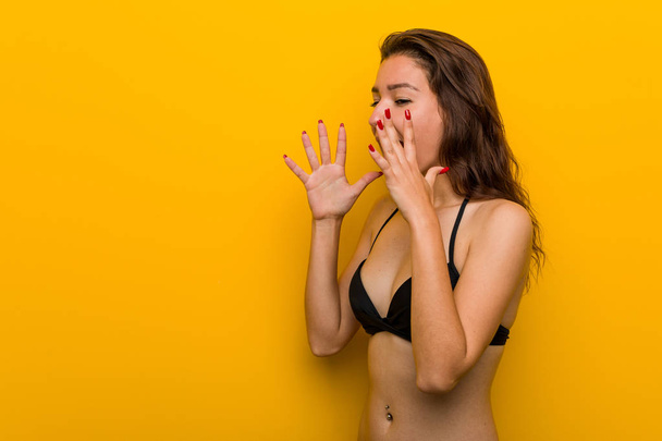 Young european woman wearing bikini shouts loud, keeps eyes opened and hands tense. - Fotografie, Obrázek