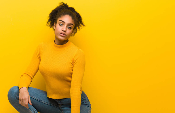 Young black woman sitting over an orange wall - Photo, Image