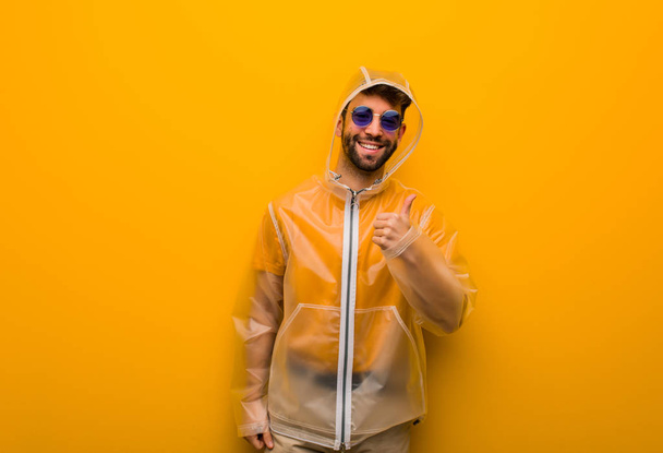 Young man wearing a rain coat smiling and raising thumb up - Photo, Image