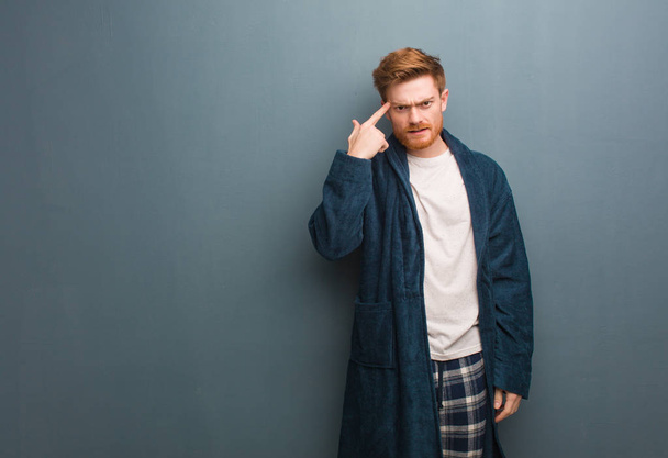 Young redhead man in pajama doing a disappointment gesture with finger - Fotografie, Obrázek