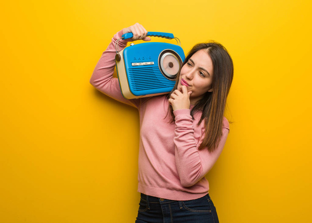 Joven linda mujer sosteniendo una radio vintage dudando y confundida
 - Foto, Imagen