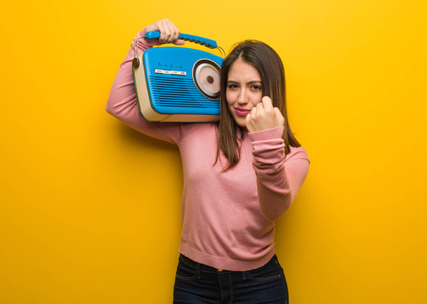 Young cute woman holding a vintage radio showing fist to front, angry expression - Photo, Image