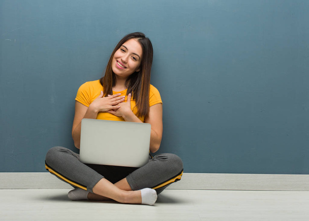 Молодая женщина сидит на полу с ноутбуком и делает романтический жест
 - Фото, изображение
