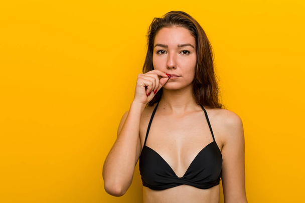 Joven mujer europea usando bikini con los dedos en los labios manteniendo un secreto
. - Foto, Imagen