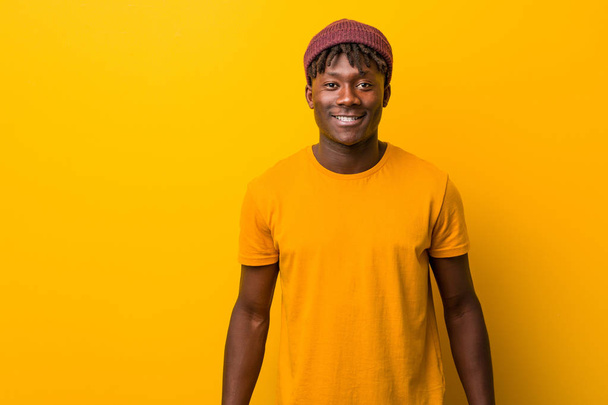 Giovane uomo nero che indossa rasta su sfondo giallo felice, sorridente e allegro
. - Foto, immagini