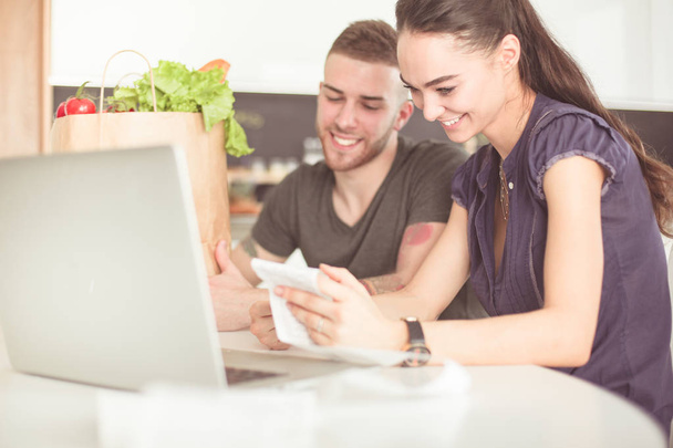 Couple paying their bills with laptop in kitchen at home - Photo, Image