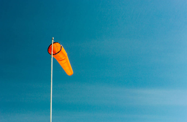 Açık mavi gökyüzüne karşı aşağı açılı düz turuncu windsock. - Fotoğraf, Görsel