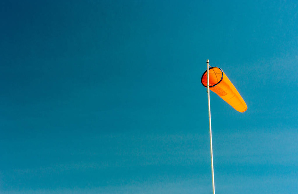 Ένας απλός πορτοκαλί ανεμοκάλτσα με καθοδική κλίση σε ένα καθαρό γαλάζιο ουρανό. - Φωτογραφία, εικόνα