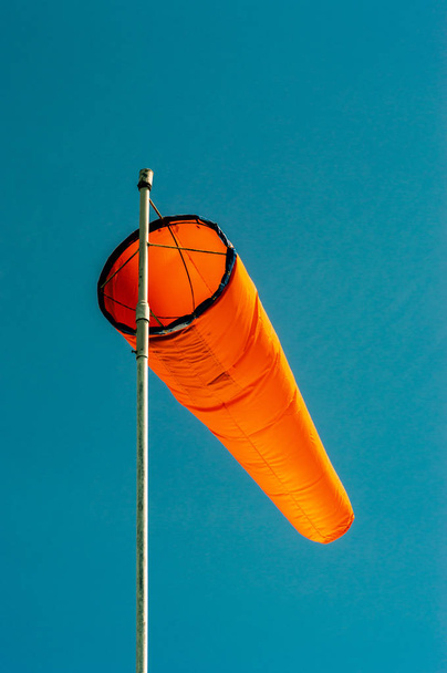 Neerwaartse schuine effen oranje windsok tegen een heldere blauwe hemel. - Foto, afbeelding