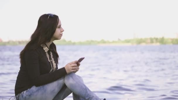 A beautiful woman using smartphone on river bank - 映像、動画