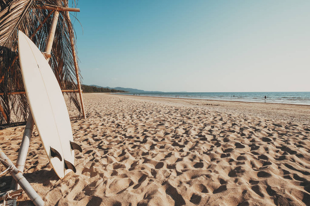 Доска для серфинга на песчаном пляже на фоне спокойного моря и неба. летние каникулы фон и водные виды спорта концепции. Эффект винтажного тона
. - Фото, изображение