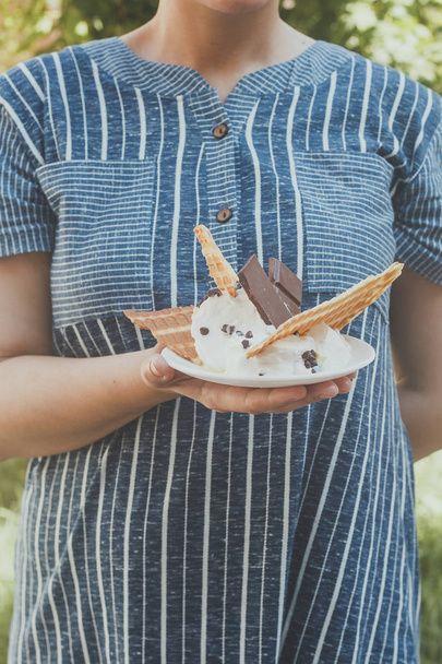 Młoda kobieta trzyma pyszne lody z goframi podczas pikniku na łonie natury. Koncepcja letniego jedzenia. Młoda dorosła osoba je pyszne lody z patykiem w pogodny letni dzień. - Zdjęcie, obraz