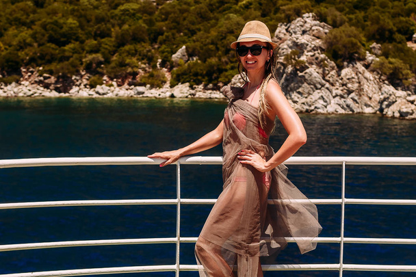 junge lächelnde Frau mit Hut und Badeanzug, die auf einer Jacht im Meer steht und in die Kamera schaut, Türkei - Foto, Bild