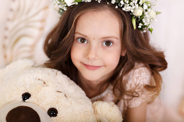 Portrait of a cute little girl with a crown from flowers on her head looking at the camer. Happy childhood concept. Close-up - Foto, immagini