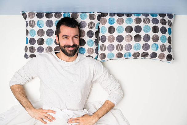 Man in bed in top view posing with arms at hip and smiling - Foto, Bild