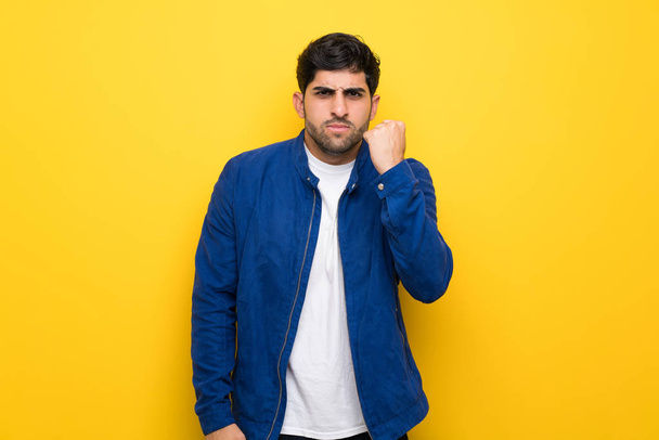 Mann mit blauer Jacke über gelber Wand mit wütender Geste - Foto, Bild