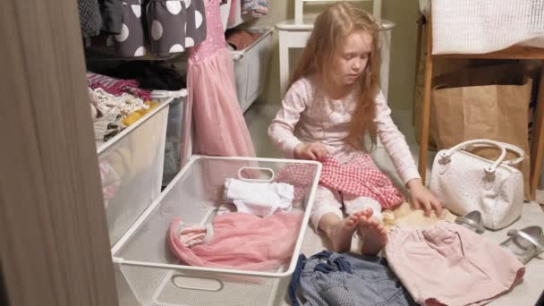 Little girl cleans up clothes in home wardrobe - Footage, Video