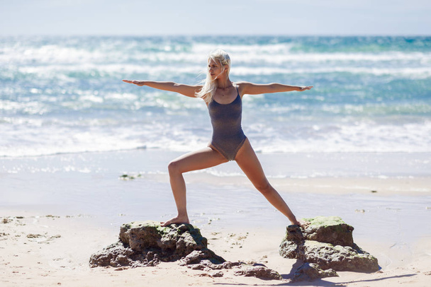 Valkoihoinen blondi nainen harjoittelee joogaa rannalla
 - Valokuva, kuva