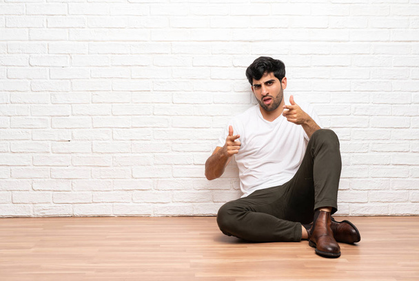 Young man sitting on the floor pointing to the front and smiling - Photo, image