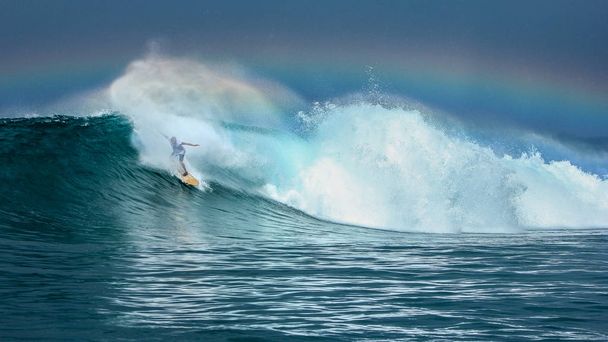 Surfista cabalgando gran ola verde con arco iris en el fondo en las islas del norte de Maluku, Indonesia
 - Foto, Imagen