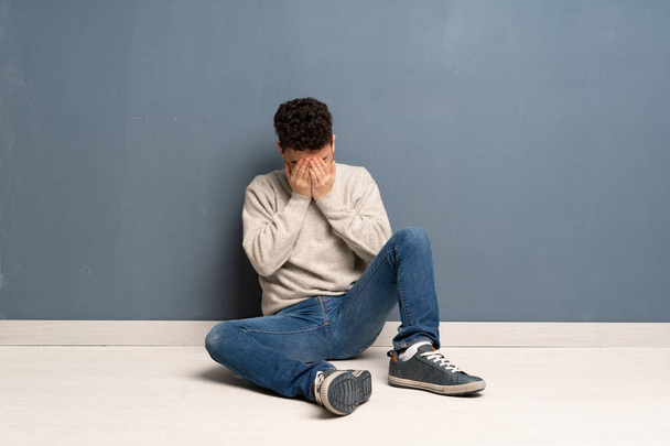 Jonge man zittend op de vloer met vermoeide en zieke expressie - Foto, afbeelding
