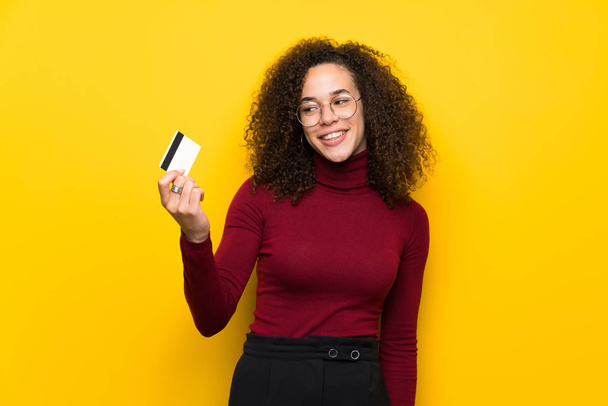 Mulher dominicana com camisola gola alta segurando um cartão de crédito e pensando
 - Foto, Imagem