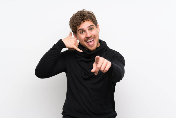Blonde man over isolated white wall making phone gesture and pointing front - Photo, Image