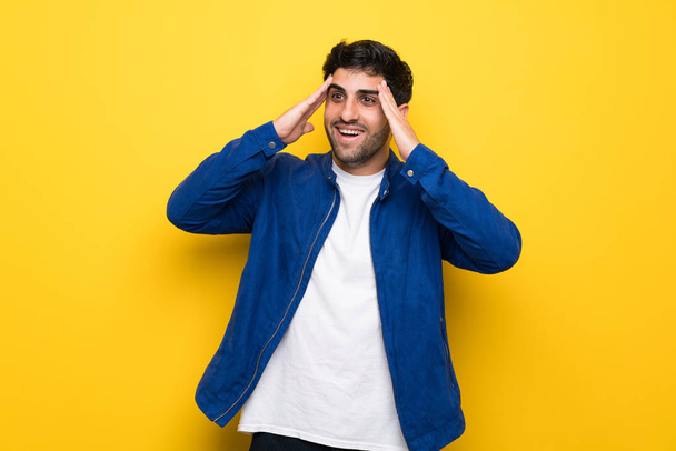 Man with blue jacket over yellow wall with surprise expression - Photo, Image