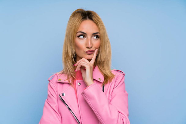 Young blonde woman with pink jacket over isolated blue background Looking front - 写真・画像