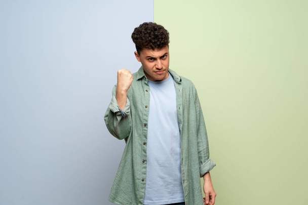 Junger Mann über blauem und grünem Hintergrund mit wütender Geste - Foto, Bild