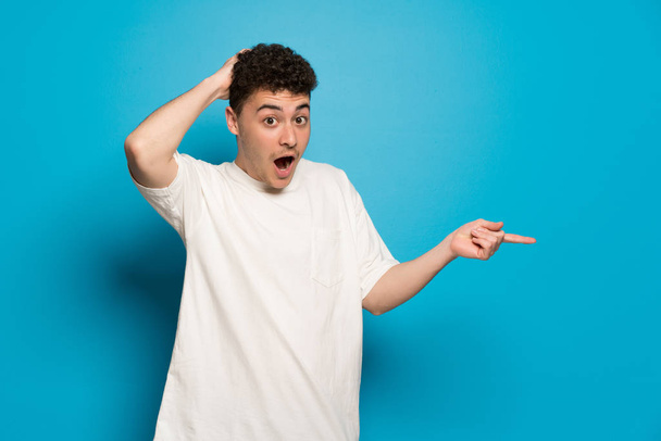 Young man over blue background pointing finger to the side and presenting a product - Photo, Image