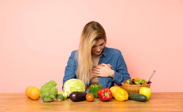 Jonge blonde vrouw met veel groenten met een pijn in het hart - Foto, afbeelding
