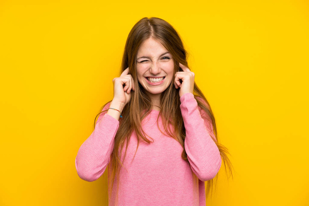 Молода жінка з довгим волоссям над ізольованою жовтою стіною розчарована і прикриває вуха
 - Фото, зображення