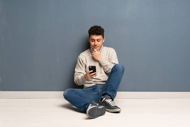 Young man sitting on the floor thinking and sending a message - Фото, зображення
