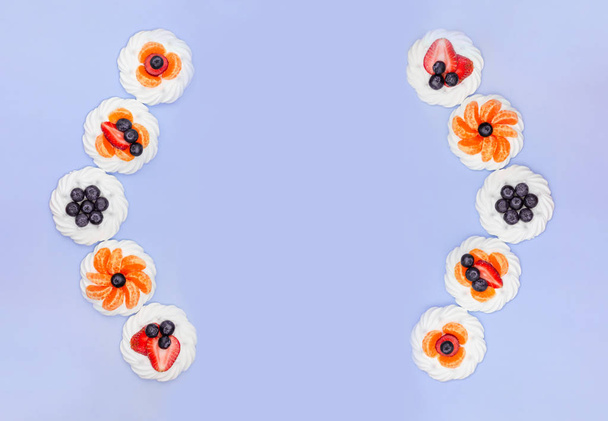 Frame of meringue with blueberries, strawberries and tangerines on a lavender background. Top view - Foto, immagini
