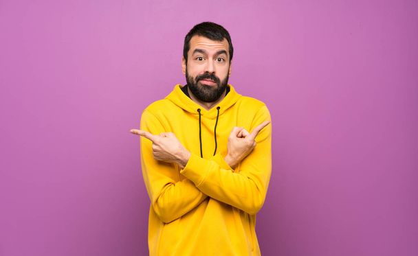 Handsome man with yellow sweatshirt pointing to the laterals having doubts - Photo, Image