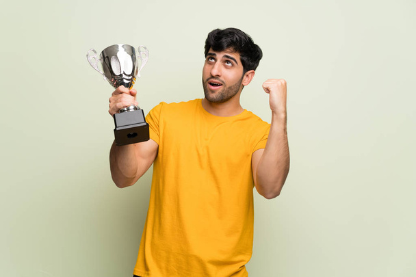 Young man over pink wall holding a trophy - Photo, image